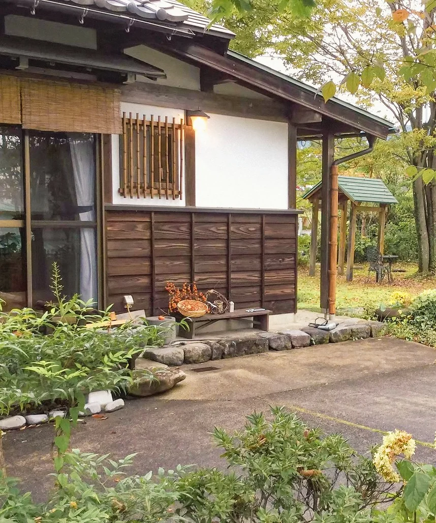縁側のベンチと格子窓のある平屋の母屋、奥に庭の東屋